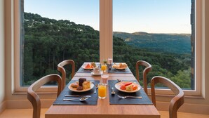 A dining table with breakfast items and a scenic view of a forested landscape through large windows. - Laghetto Resort Golden (Gramado)