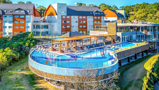 A hotel with a circular pool, multiple buildings, and a lush green landscape. - Laghetto Resort Golden (Gramado)