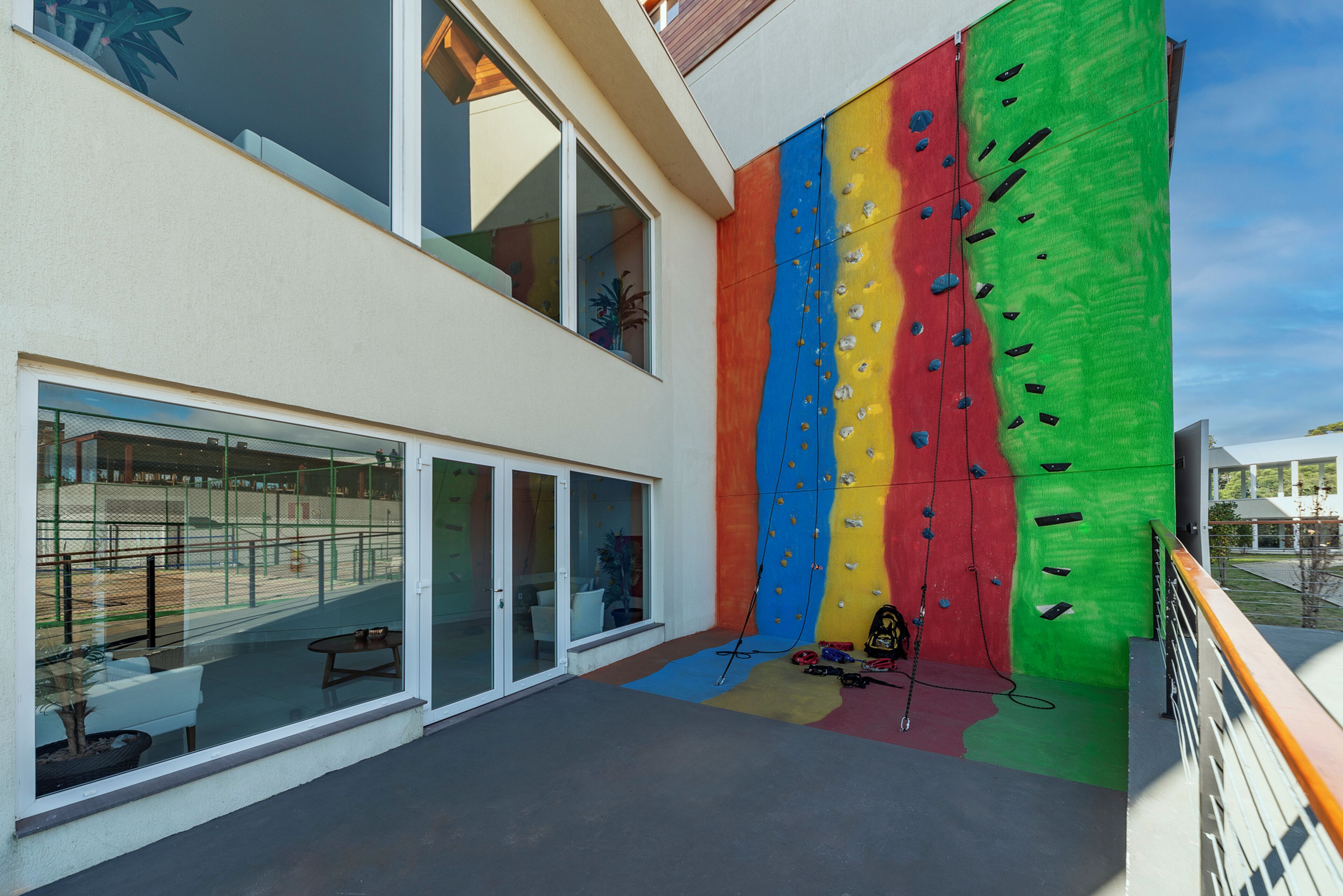 A modern building with large windows, a colorful climbing wall, and a balcony with a railing.