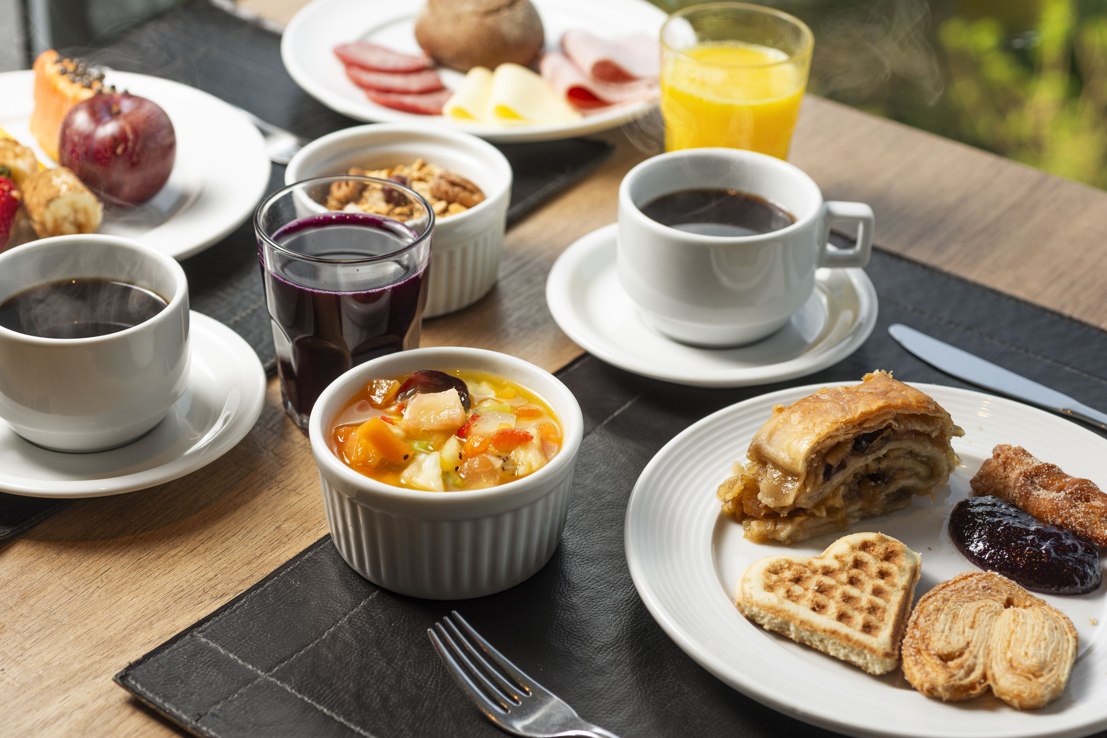 A breakfast setting with various dishes, including a bowl of soup, waffles, pastries, and a glass of orange juice.