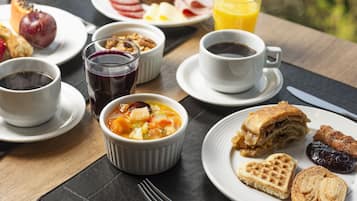 A breakfast setting with various dishes, including a bowl of soup, waffles, pastries, and a glass of orange juice.