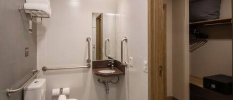 Un baño moderno con inodoro, lavamanos y ducha. Incluye barras de apoyo y ducha accesible para sillas de ruedas.