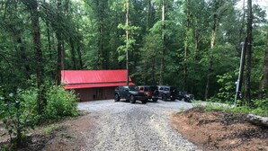 A gravel driveway leading to a red-roofed building surrounded by tall trees. - LIAHN CABIN AT WINDROCK RIDGE .RIDE TO THE TRAILS IN A MINUTE, RIDE,RELAX,REPEAT (Oliver Springs)