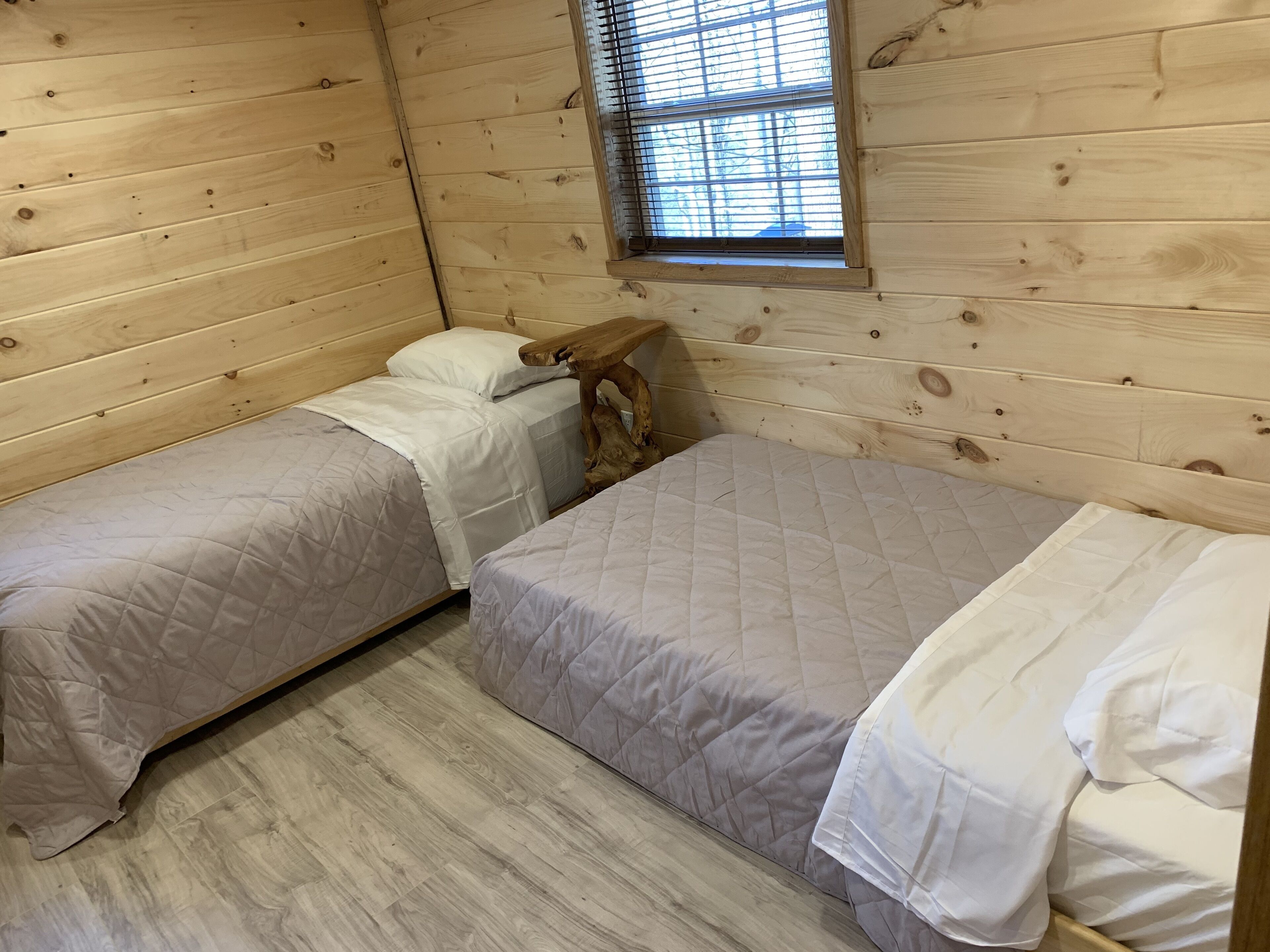 A small, cozy room with two beds, wooden walls, a window, and a wooden headboard.