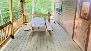 A wooden deck with a picnic table and benches, surrounded by a forested area. - LIAHN CABIN AT WINDROCK RIDGE .RIDE TO THE TRAILS IN A MINUTE, RIDE,RELAX,REPEAT (Oliver Springs)