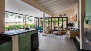 Una cocina amplia con una isla grande, un comedor con sillas de mimbre y vistas a la vegetación exterior.