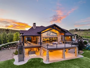 Une maison moderne à deux étages, dotée d’une grande terrasse, d’un espace salon extérieur et de fondations en pierre.