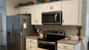 Una cocina con armarios blancos, un refrigerador de acero inoxidable, microondas, horno y encimeras de granito.