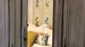 Een slaapkamer met een bed, kussens en een spiegel die bloemen behang weerkaatst.
