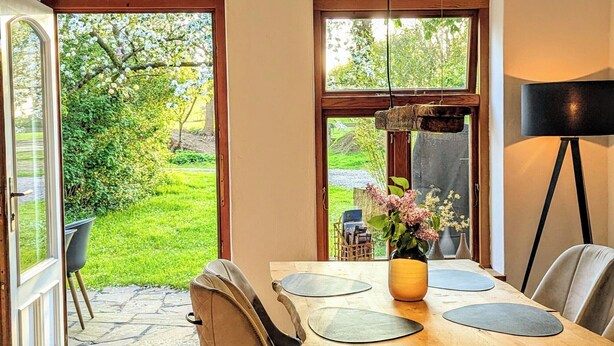 A dining area with a wooden table, chairs, a vase with flowers, and a lamp. - Ferienwohnung auf Einem Resthof (Quickborn)