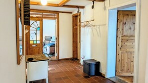 A hallway with a tiled floor, wooden beams, a ceiling light, a coat rack, and a door with a wooden panel. - Ferienwohnung auf Einem Resthof (Quickborn)