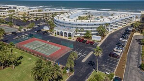 Un hotel sul lungomare con un edificio a forma circolare, un campo da tennis e un parcheggio.