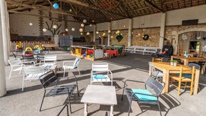Un espace extérieur aménagé en terrasse, avec des tables et des chaises, un mur en pierre et des guirlandes lumineuses.