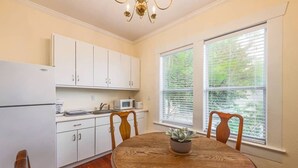 A kitchen with white cabinets, a microwave, and a sink. There is a dining table with chairs and a potted plant. - 6 Bedrooms in #1 Central Location (Austin)