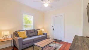 A living room with a grey sofa, two yellow patterned cushions, a wooden coffee table, a white door, and a ceiling fan. - 6 Bedrooms in #1 Central Location (Austin)