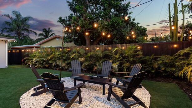 An outdoor seating area with Adirondack chairs and a table, surrounded by a wooden fence and a variety of plants. - !! Modern & Stylish Fort Lauderdale Getaway !! (Fort Lauderdale)