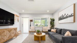 A modern living room with a grey sofa, a round coffee table, and a TV mounted on the wall. - !! Modern & Stylish Fort Lauderdale Getaway !! (Fort Lauderdale)