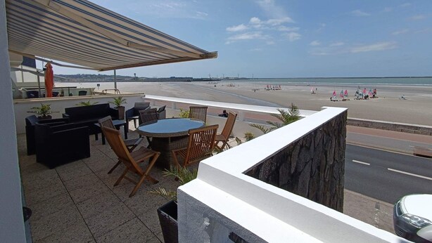 Une terrasse avec des sièges extérieurs, une vue sur la plage et un ciel dégagé.