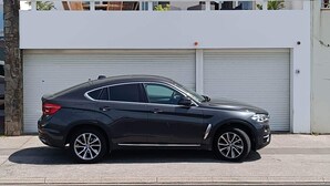 Une voiture noire est garée devant un immeuble moderne doté d’un portail de garage et d’un balcon orné de plantes.