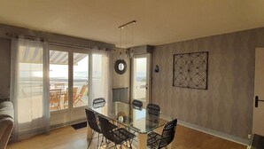 Un coin repas avec une table et des chaises en verre, une vue dégagée grâce à de grandes fenêtres et une porte donnant sur l’extérieur.
