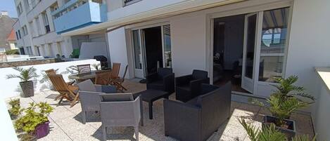 A terrace with outdoor furniture, potted plants, and a view of the building's interior.