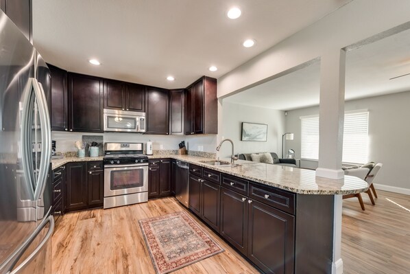 Una cocina moderna con armarios de madera oscura, electrodomésticos de acero inoxidable, encimera de granito y suelo de madera.