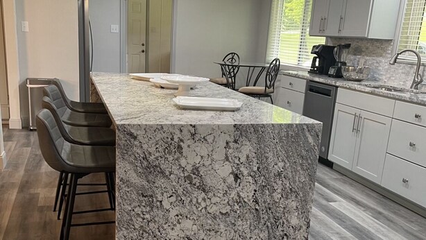 A modern kitchen with a large island, bar stools, a coffee maker, and a dishwasher.