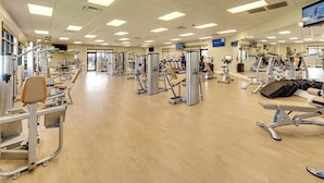 Ein geräumiger Fitnessraum mit verschiedenen Trainingsgeräten, Spiegeln und einem Fernsehbildschirm.