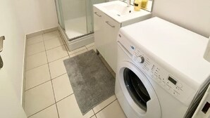 Une salle de bain compacte avec une douche à parois de verre, un lave-linge et un lavabo avec un miroir au-dessus.