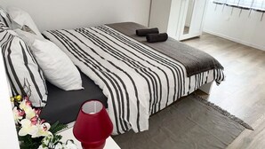 Une chambre à coucher moderne avec une couvre-lit à rayures, un tapis gris et une lampe rouge posée sur une table de chevet.