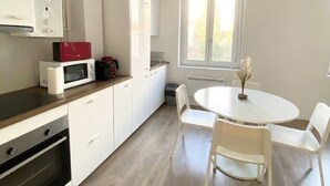 Une cuisine moderne avec des armoires blanches, un four à micro-ondes et une cuisinière. On y trouve une table à manger avec quatre chaises et un luminaire suspendu.