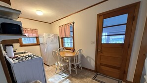 Cocina compacta con estufa a gas, refrigerador y mesa de comedor con sillas.