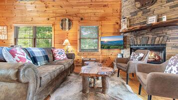 A cozy cabin interior with a wooden ceiling, a fireplace, a sofa, and a coffee table.
