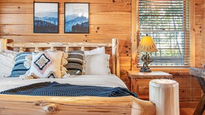 Une chambre à coucher dans une cabane en bois, avec un lit, des oreillers, une lampe et deux tableaux encadrés au mur.