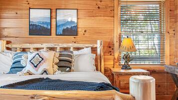A wooden cabin bedroom with a bed, pillows, a lamp, and two framed pictures on the wall.