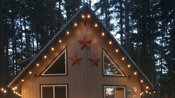 Una cabana amb façana de fusta, un porxo amb llums de garlandes i una decoració d'estrella al frontal.