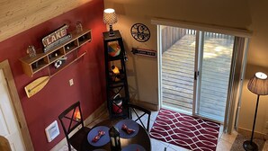 Zona de menjador amb un sostre alt, una paret vermella, una estanteria de fusta amb ampolles, un cartell que diu "Lake Cabin Lodge" i vista d'una terrassa a través d'una porta corredissa.