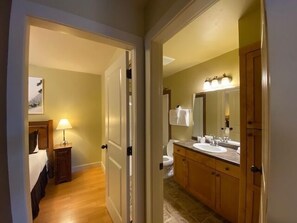Habitación de hotel con cama, mesita de noche, lámpara y vista al baño.