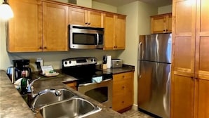 A kitchen with wooden cabinets, a stainless steel sink, a microwave, a toaster, and a refrigerator.