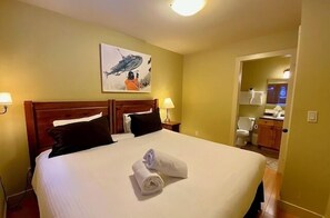 Habitación de hotel con una cama grande, dos lámparas de noche, un cuadro en la pared y un baño visible a través de una puerta abierta.
