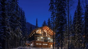 Eine mehrstöckige Blockhütte mit großen Fenstern und einem Balkon, umgeben von schneebedeckten Bäumen.