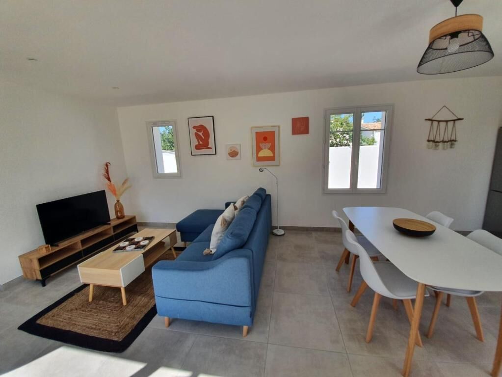 Ein modernes Wohnzimmer mit blauem Sofa, Fernseher, Esstisch und Kunstwerken an den Wänden.