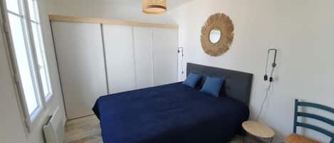 Une chambre à coucher avec un lit, une chaise, un miroir rond et un luminaire suspendu.