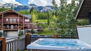 Ein Whirlpool mit Bergblick, eine Holzterrasse und ein zweistöckiges Gebäude mit Balkonen.