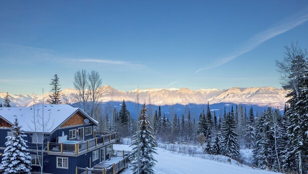 Eine zweistöckige Lodge mit Balkon, umgeben von schneebedeckten Bäumen und Bergen im Hintergrund.