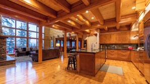Un intérieur spacieux de chalet en bois, avec une grande cuisine, des planchers en bois et un salon confortable doté d’une cheminée.