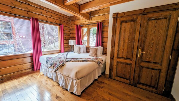 A wooden cabin bedroom with a bed, curtains, and a large wooden door.