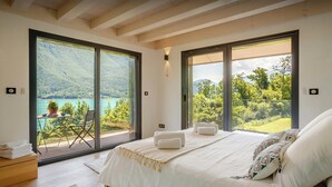 Une chambre avec un grand lit, deux fenêtres et une vue sur un lac et des montagnes.