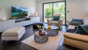 Un salon moderne doté d’un téléviseur à écran plat, de sièges confortables, d’un coin repas et d’une grande fenêtre offrant une vue sur la verdure.