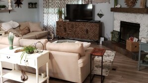 A living room with a beige sofa, a white side table, a wooden cabinet, a television, a fireplace, and a ceiling fan.